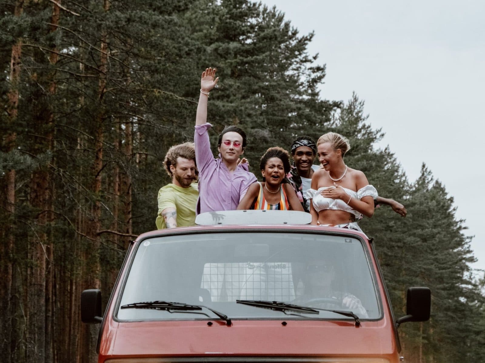 Un groupe d'amis debout dans un van rouge, sur une route en forêt